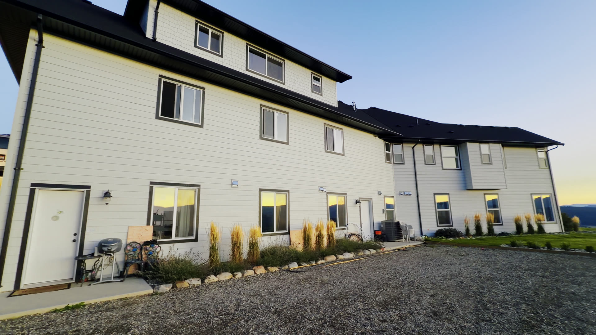 The house at sunset: white siding, black roof and trim, ornamental grasses along the front