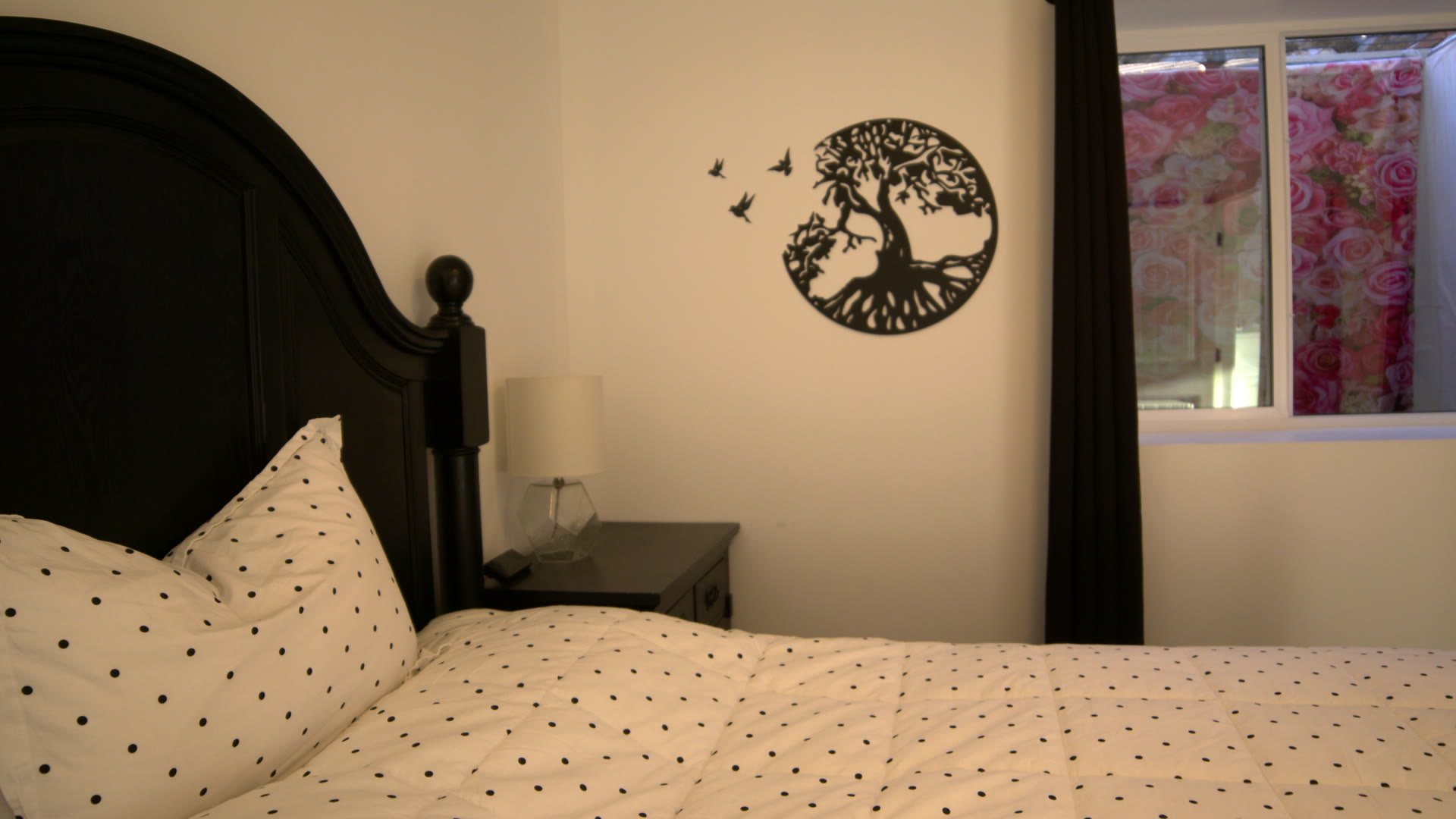 Bedroom: dark wood headboard, polka-dot duvet, two lamps and the tree on the wall in the afternoon sun