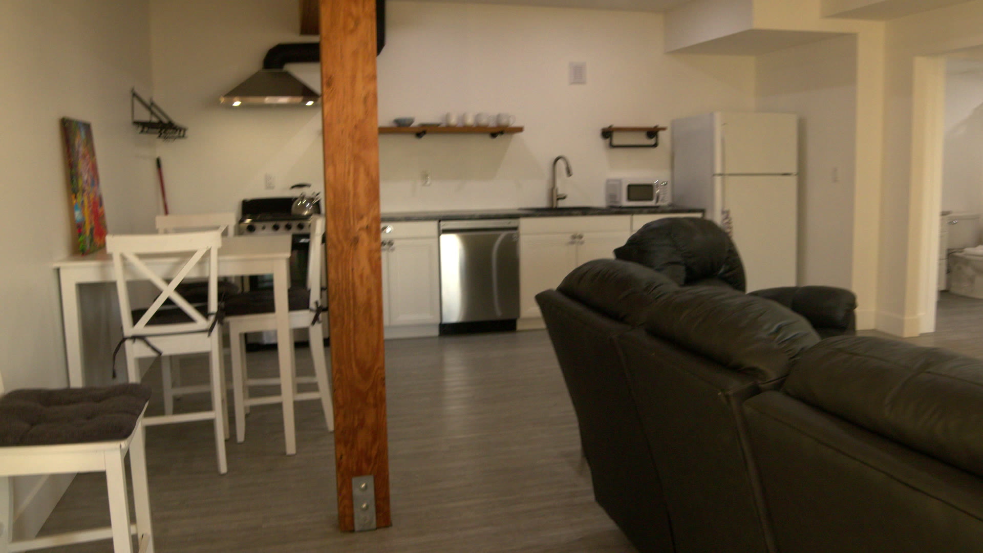Suite See living room and kitchen: leather couches, the timber post, white cabinets and dark counter